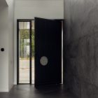 Bespoke black steel door with a circular cut-out opens into a modern interior, featuring large windows and textured grey wall panels.