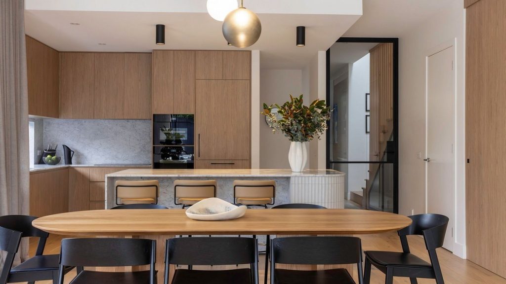 Modern kitchen and dining area featuring a wooden table, black chairs, sleek cabinetry, marble accents, and a floral arrangement.