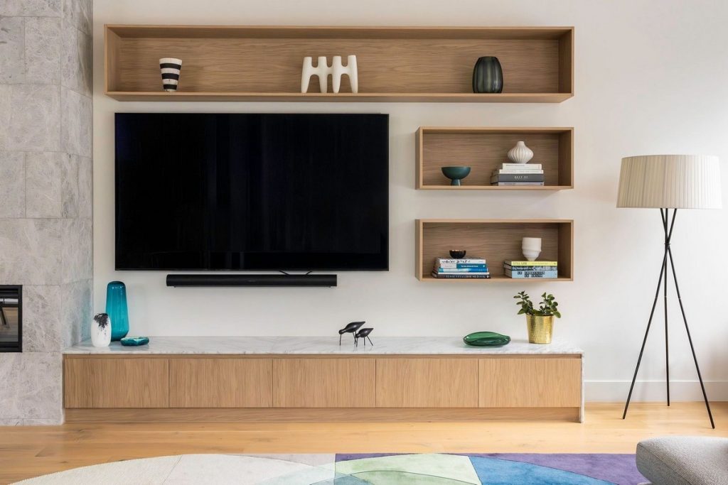 Sleek living room with a mounted TV, minimalist wooden shelves, stylish decor items, and a modern floor lamp, featuring a colourful rug.