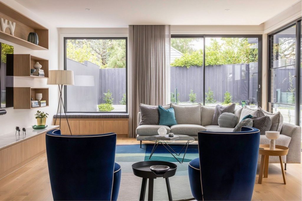 Modern living space featuring a light grey sofa, blue accent chairs, and large windows overlooking a green garden, creating a serene atmosphere.