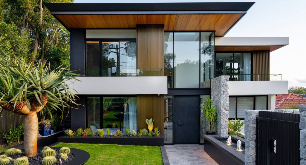 Contemporary two-storey house featuring a mix of black, wood, and white cladding, surrounded by lush greenery and modern landscaping.