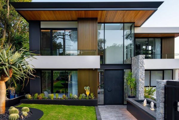 Contemporary two-storey house featuring a mix of black, wood, and white cladding, surrounded by lush greenery and modern landscaping.
