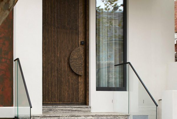 Bespoke architectural entrance featuring a textured bronze door, large glass panel, and sleek black railings on stone steps.