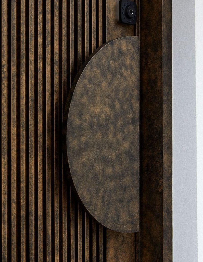 Bronze-toned textured door featuring vertical slats and a modern circular handle, emphasising sleek design and craftsmanship.