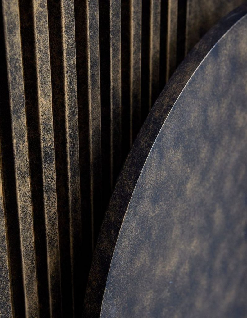 Textured, dark-toned materials showcase a circular shape next to vertical striped panels, emphasising architectural design elements.