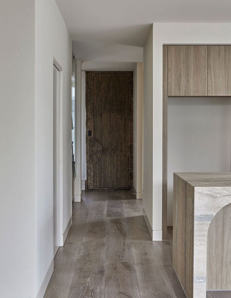 A modern hallway featuring a textured brown door, light wood cabinetry, and smooth grey flooring, creating a sleek and minimalist aesthetic.