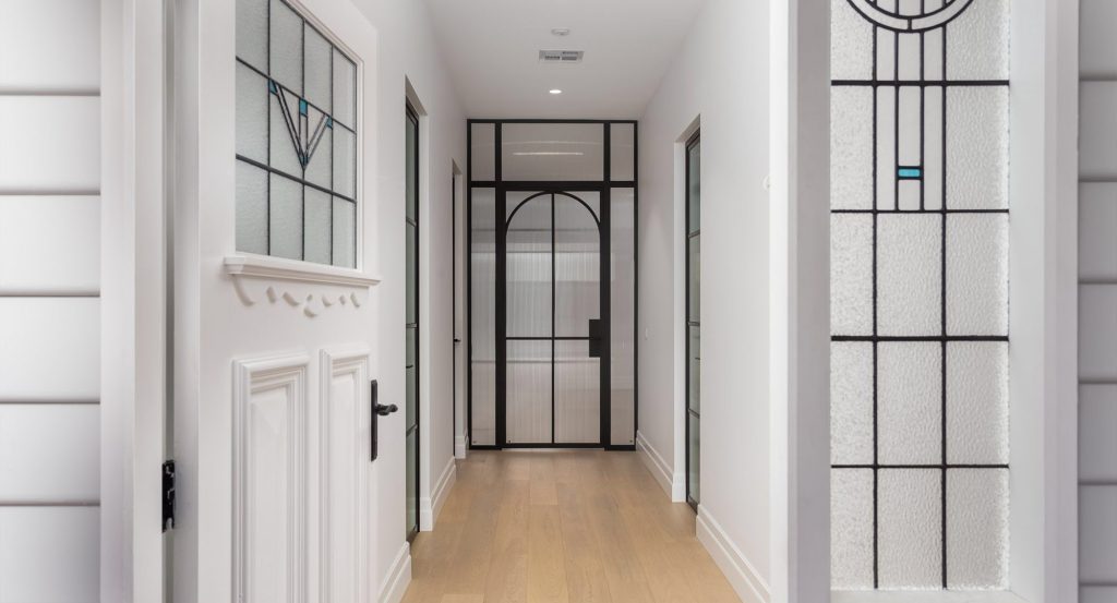 Elegant hallway featuring black steel-framed doors and windows, white walls, and light wooden flooring, creating a modern ambience.
