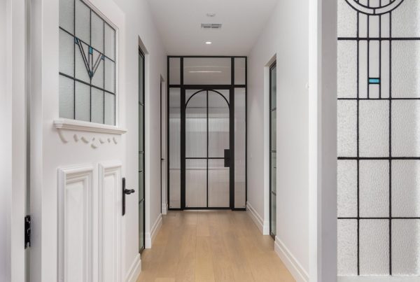 Elegant hallway featuring black steel-framed doors and windows, white walls, and light wooden flooring, creating a modern ambience.