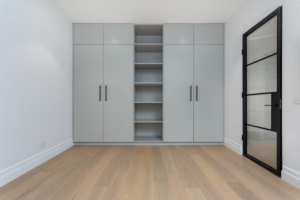 Modern interior featuring sleek grey cabinetry with multiple shelves and a black steel-framed door, set against light wood flooring.