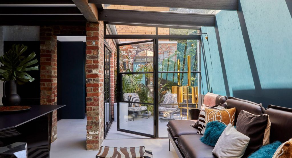 Bright courtyard space featuring large steel-framed glass doors, exposed brick walls, and modern furnishings, enhancing indoor-outdoor flow.