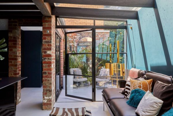 Bright courtyard space featuring large steel-framed glass doors, exposed brick walls, and modern furnishings, enhancing indoor-outdoor flow.