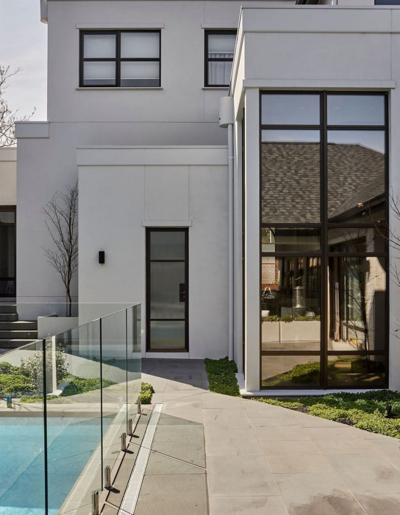 Modern residence exterior featuring sleek steel-framed glass doors, minimalist design elements, and a clear pool alongside lush greenery.