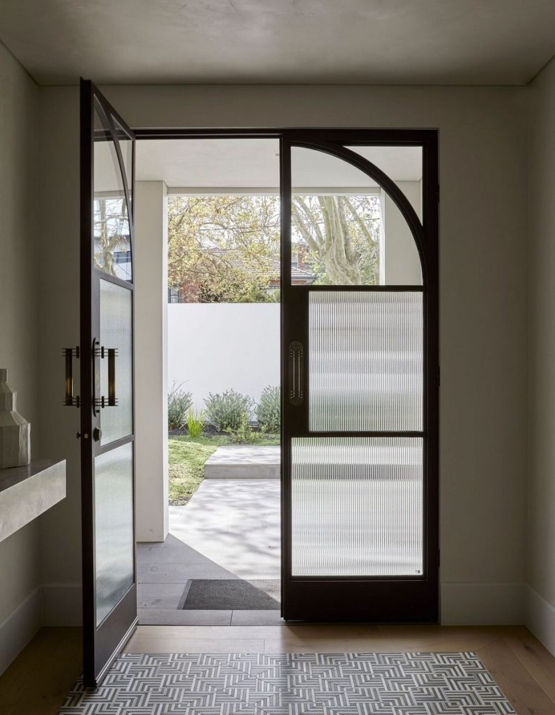 Bespoke steel door with an arched top, partially open to reveal a serene garden path and greenery outside, framed by a modern interior.
