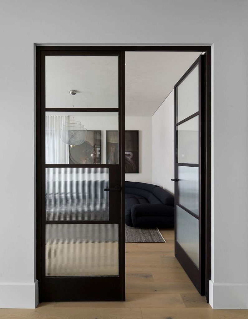 Bespoke black steel-framed sliding door with frosted glass panels, leading to a modern living space featuring a dark sofa and artwork.