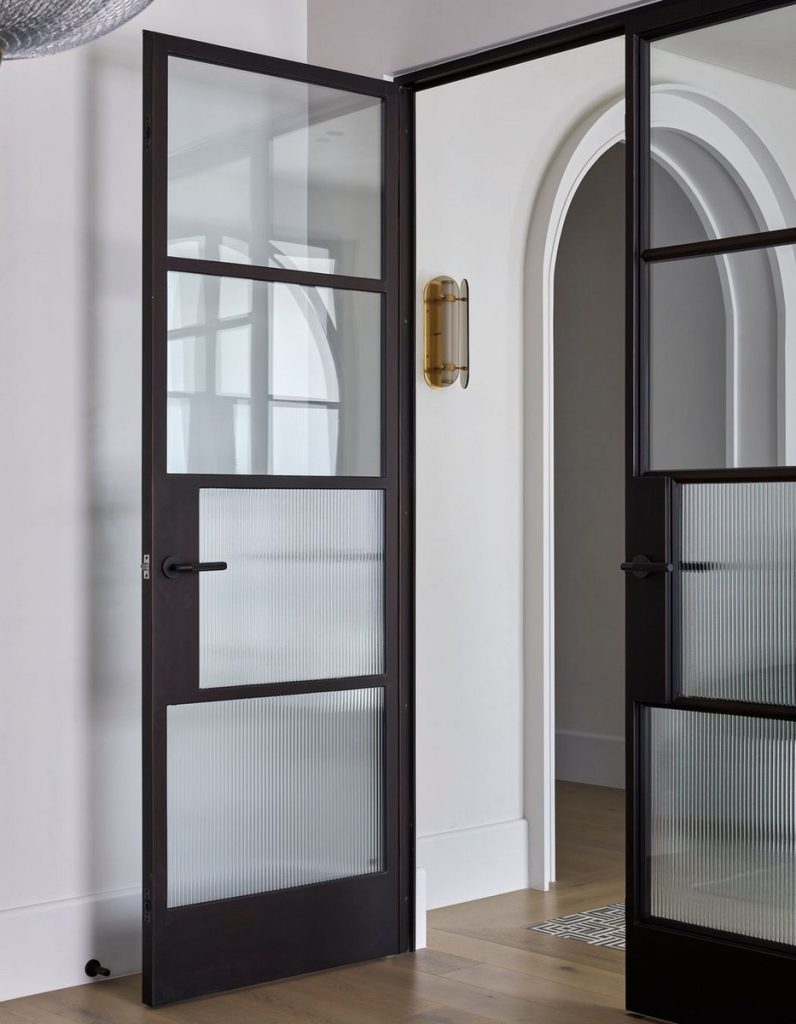 Bespoke black steel door with a translucent glass panel, framed in a modern interior featuring an arched doorway and warm wooden floor.