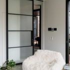 Bespoke steel sliding door with frosted glass panels divides a contemporary living space, featuring a textured white armchair and natural elements.