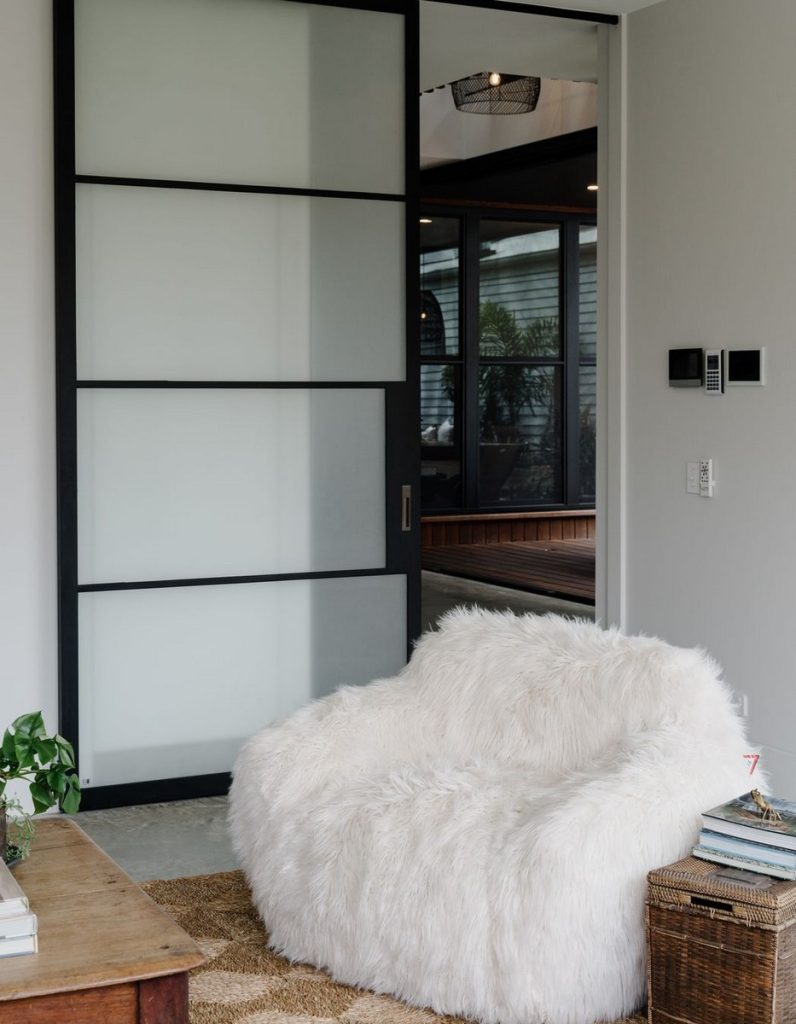 Modern interior featuring a black framed glass sliding door and a plush white armchair on a textured rug, creating a cozy space.