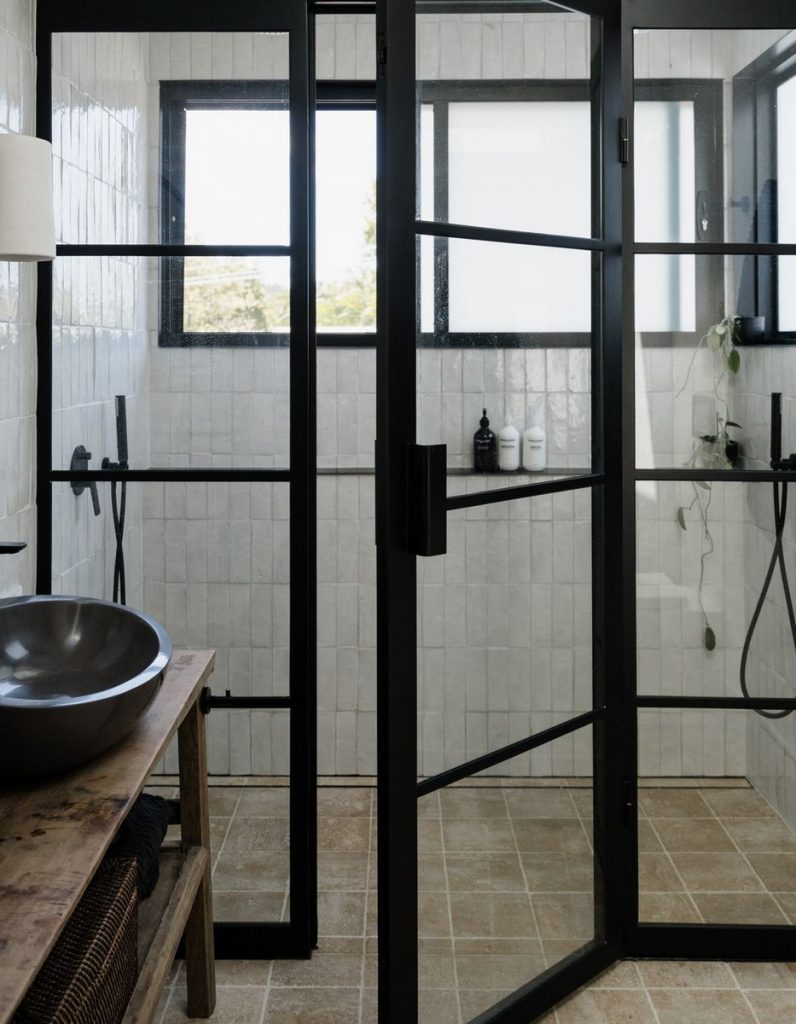 Bespoke black steel-framed shower enclosure with glass doors, wooden vanity, and modern fixtures in a light, neutral-toned bathroom.