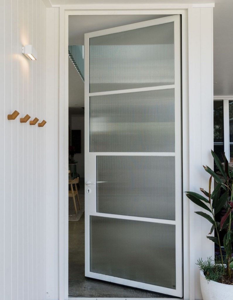 Stylish steel-framed door with frosted glass panels, set in a modern white entryway, complemented by greenery and minimalist décor.