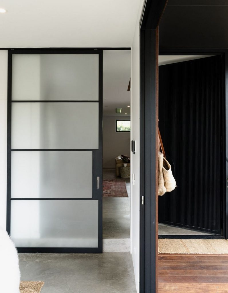 Bespoke steel door system with frosted glass panels, leading to a modern interior with wooden accents and a textured rug.