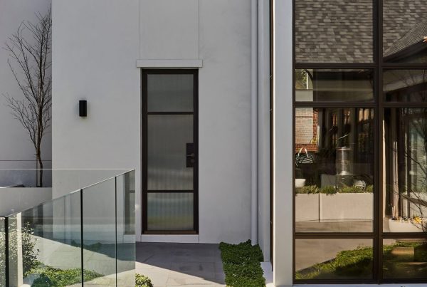 Sleek architectural design featuring a black steel door and large steel-framed glass windows, with greenery and modern finishes.