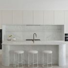 Sleek kitchen featuring a marble island, minimalist cabinetry, two built-in ovens, and three stools with a light, modern aesthetic.