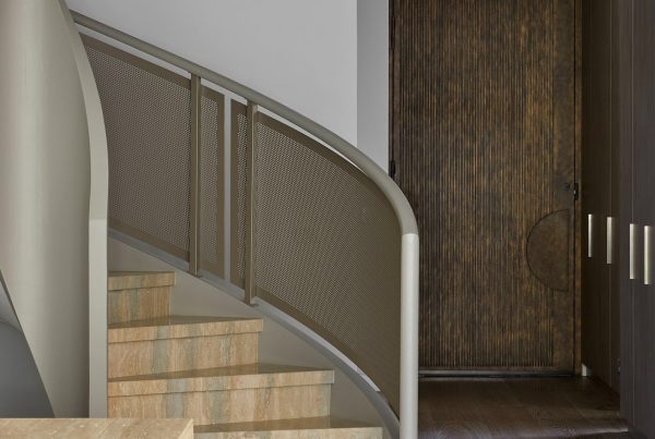 Curved staircase leading to a textured wooden door; contemporary design with neutral tones and sleek metal details.