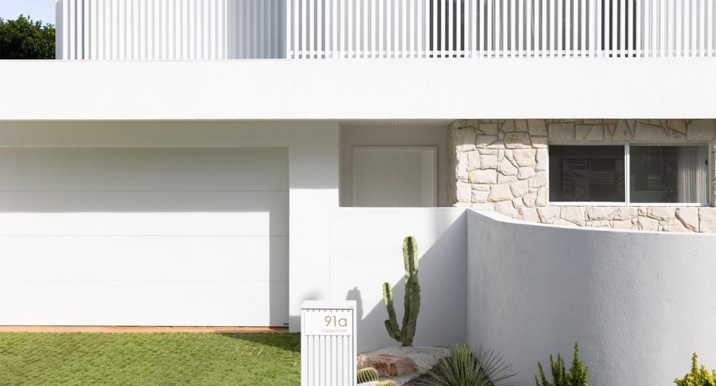 Modern white residence with a stone feature wall, green lawn, a vertical garden, and minimalist design elements, featuring garage and entry.