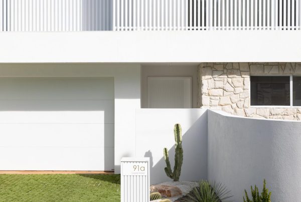 Modern white residence with a stone feature wall, green lawn, a vertical garden, and minimalist design elements, featuring garage and entry.