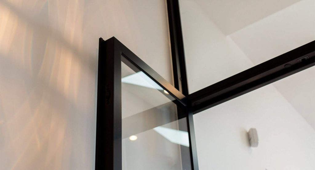 Close-up of a sleek black steel-framed glass door, showcasing clean lines and modern design against a softly lit interior.