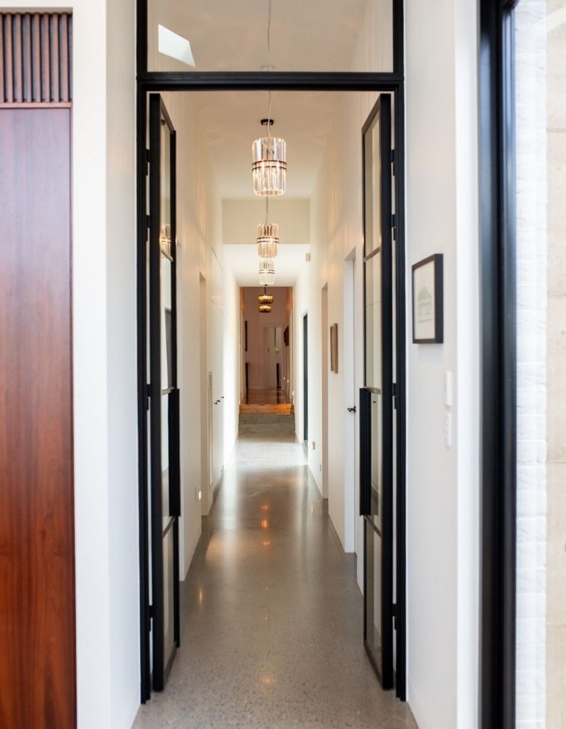 Elegant hallway featuring black steel-framed doors, polished concrete flooring, and stylish pendant lighting, creating a modern aesthetic.