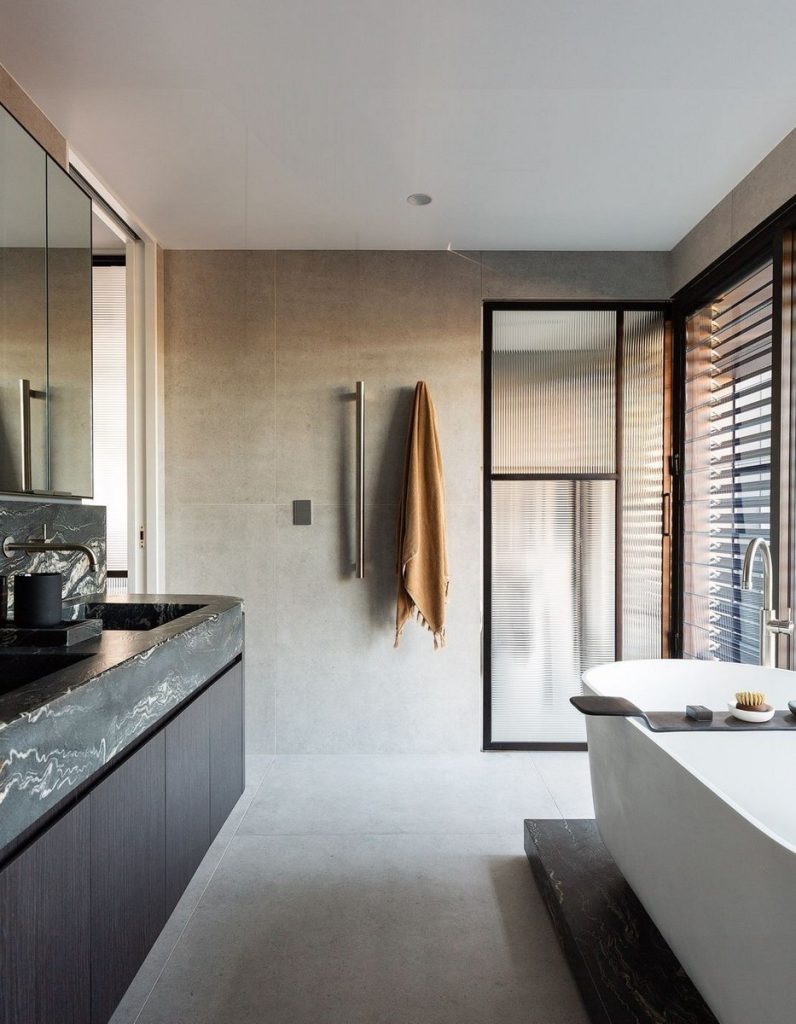 Contemporary bathroom featuring a freestanding bathtub, sleek black cabinetry, grey stone walls, and large glass windows with wooden slats.