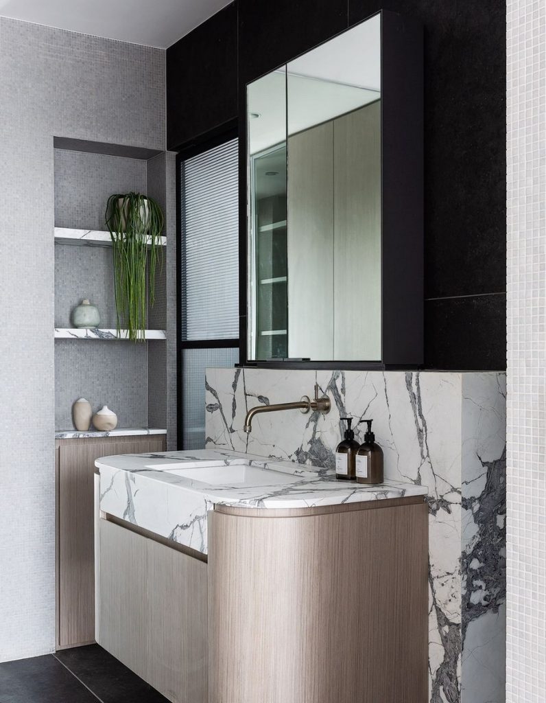 Modern bathroom with marble sink and sleek cabinetry, featuring dark and light contrasts, mirrors, and stylish decorative elements.