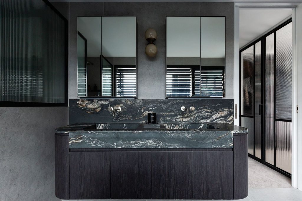 Luxurious bathroom featuring a dark marble vanity with dual mirrors, stylish lighting fixtures, and a sleek black-framed glass partition.