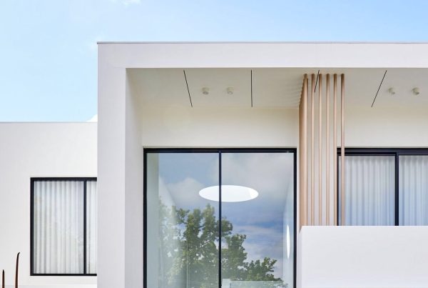 Modern white residence featuring large glass windows, sleek lines, and wooden accents against a clear blue sky.