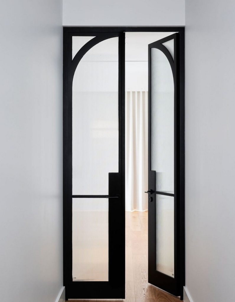 Elegant black-framed double doors with vertical glass panels, leading into a softly lit room with warm wooden flooring.