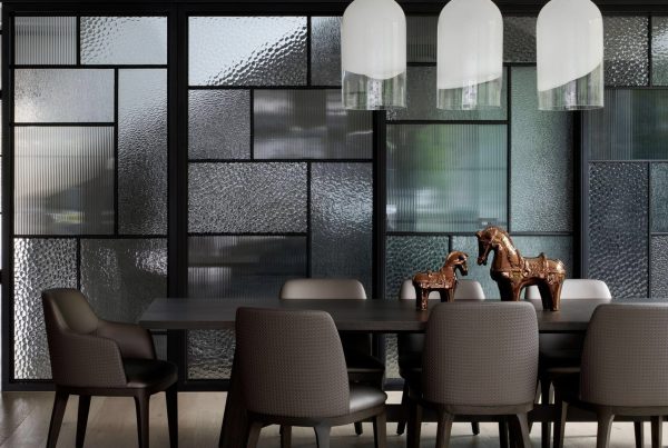 Modern dining area featuring a dark wooden table, grey upholstered chairs, and sculptural horse figurines, surrounded by textural glass partitions.