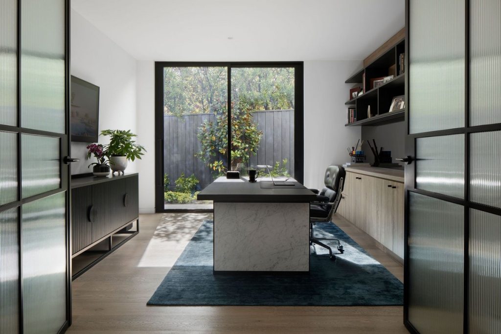 Bright, modern home office with a marble-topped desk, sleek furniture, and large glass doors opening to a garden view.