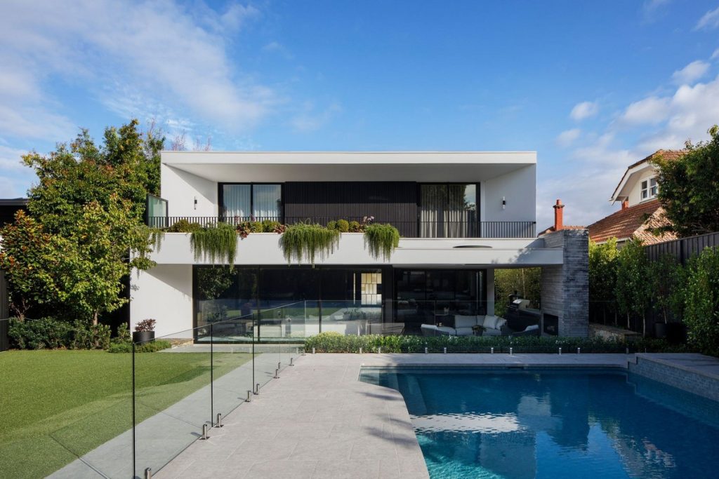 Contemporary two-storey residence with a sleek white façade, large glass windows, and a tranquil pool surrounded by greenery.