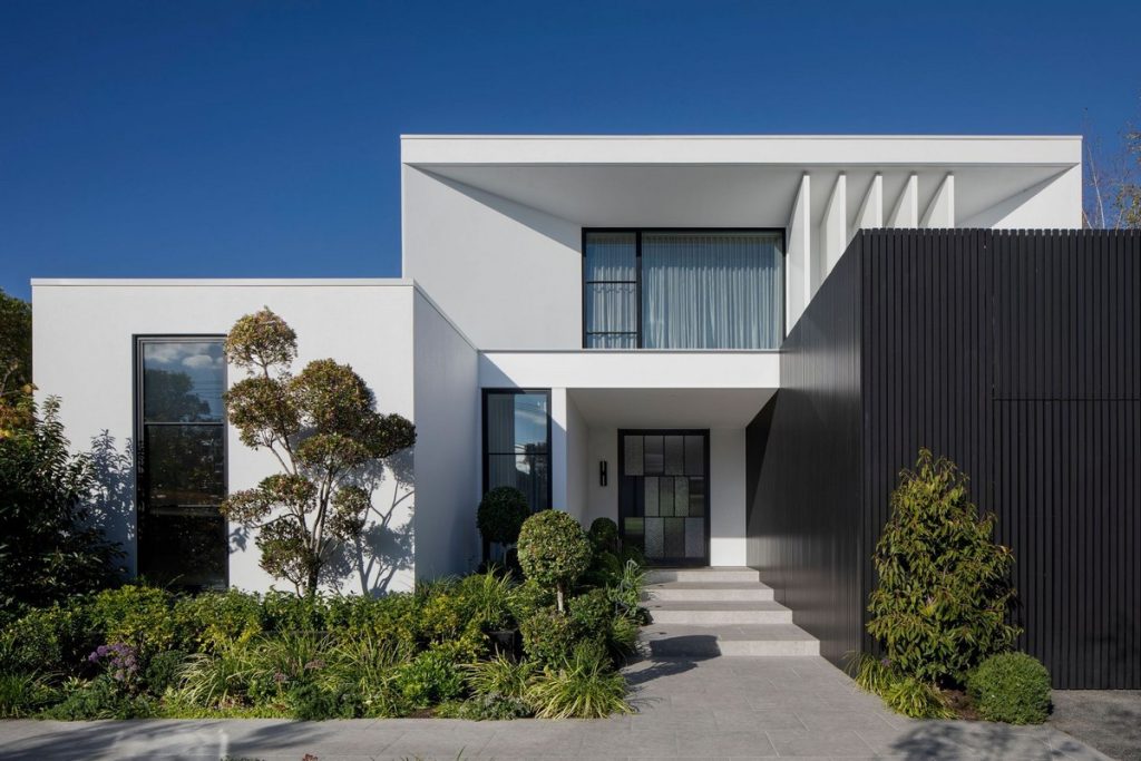 Modern white residence featuring a sleek façade, large glass windows, sculptural elements, and landscaped greenery.