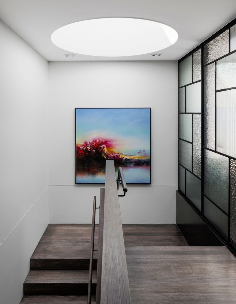 Bright, modern staircase leading to a round skylight, featuring a vibrant artwork and sleek glass partitions.