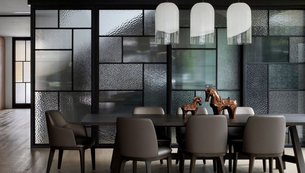Modern dining area featuring a dark wood table, upholstered chairs, and decorative horse sculptures, framed by textured glass partitions.