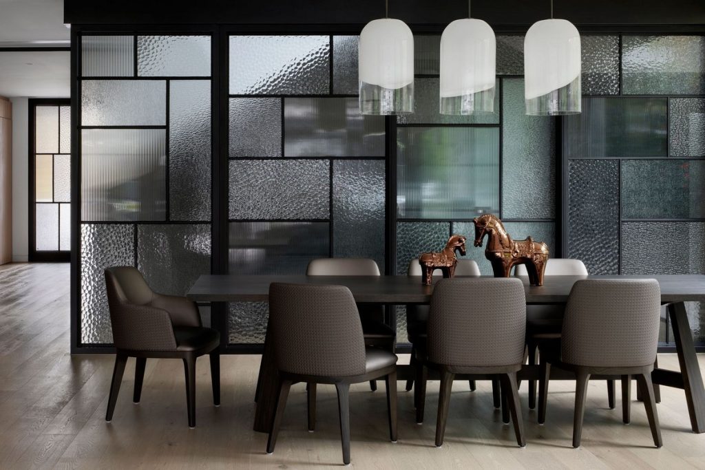 Contemporary dining area featuring a dark wooden table, upholstered chairs, and glass-panelled partitions with a textured finish.