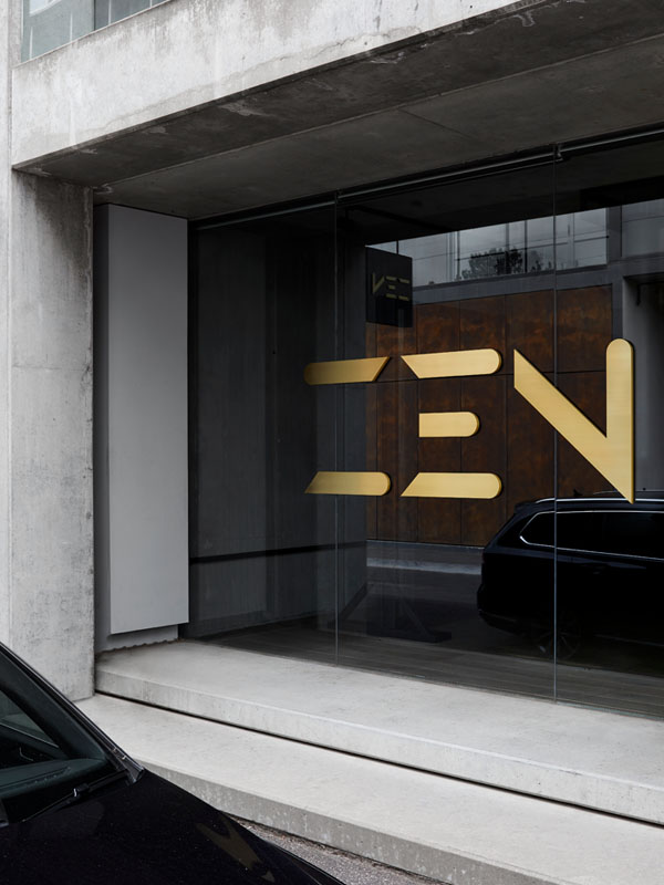 Gold lettering spelling "ZEN" on a glass facade, framed by concrete walls, with a dark car parked outside.