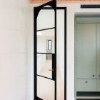 Black steel-framed glass door with an arched top, partially open, leading into a bright interior featuring light wood flooring.