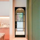 Steel-framed glass hinge door in a modern interior, featuring a black frame, arched top, and surrounded by light-coloured walls and cabinetry.