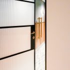Glazed steel-hinge door with frosted panels, showcasing a modern interior with a tiled floor and elegant metallic handles.