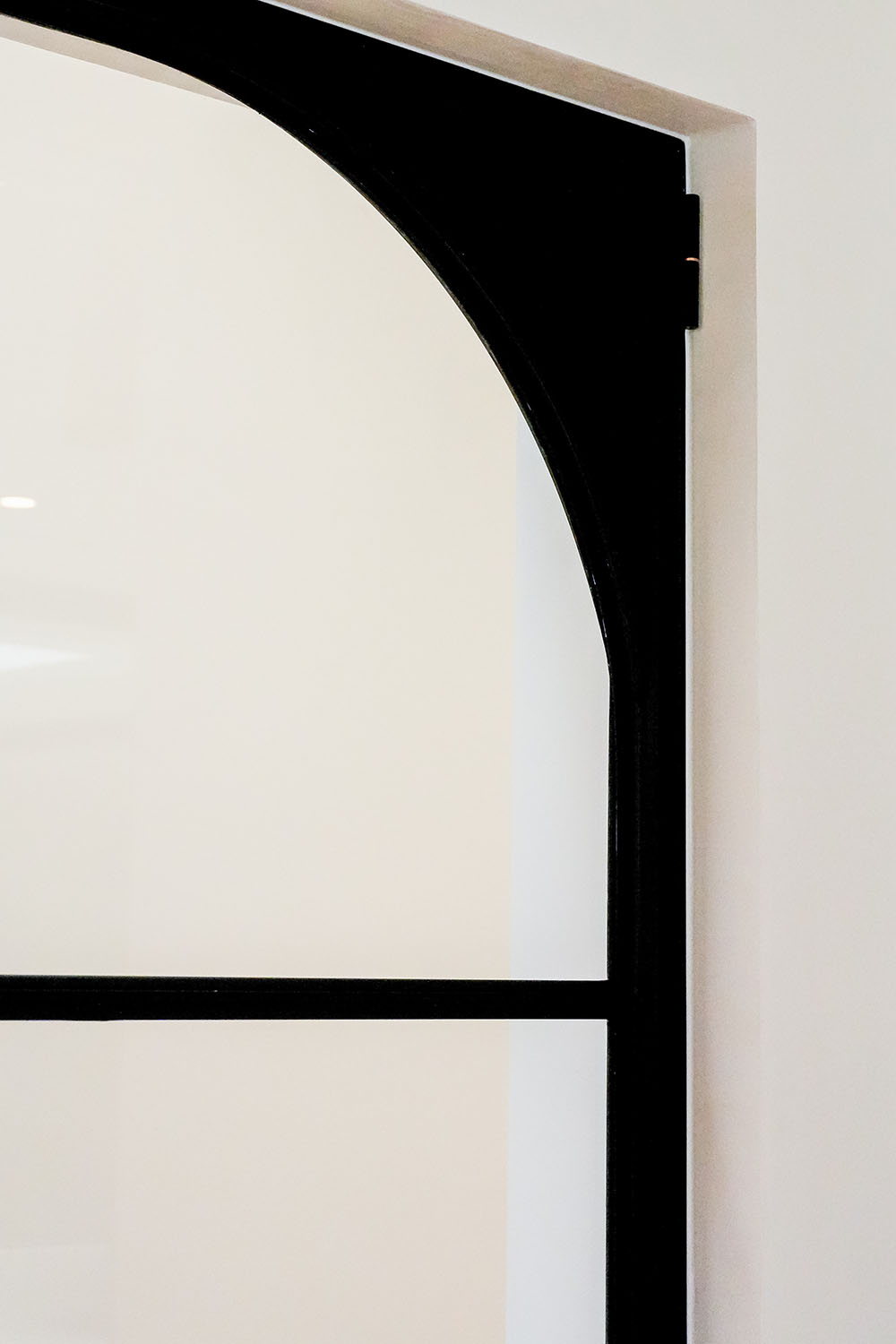 Black steel-framed glass door with an elegant arch design, set against a minimalist white wall, highlighting modern architectural style.