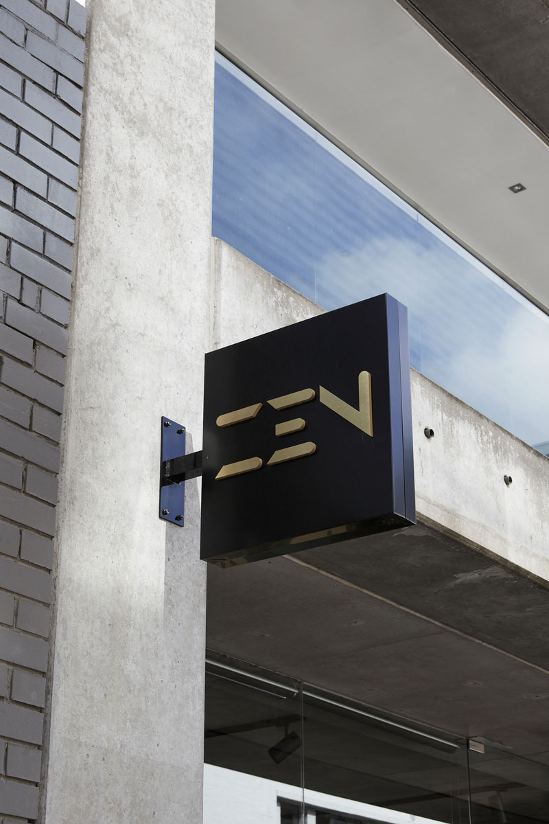 Stylish black and gold sign displaying "ZEN" mounted on a textured concrete wall, set against a modern glass façade.