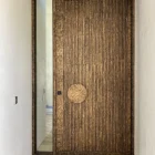 Bespoke iron pivot entry door with vertical grooves and a circular handle, complemented by a narrow glass panel beside it.